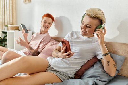 Lesbian couple with short hair spend quality time playing games together on a cozy bed in their bedroom.