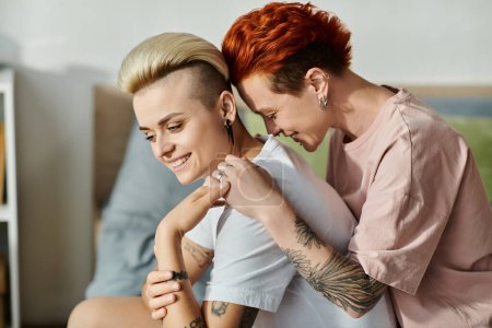 Foto de Pareja de lesbianas con el pelo corto abrazándose cariñosamente en una cama acogedora en un dormitorio, expresando amor y abrazando su estilo de vida LGBT. - Imagen libre de derechos