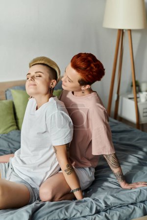 Zwei Frauen, ein lesbisches Paar mit kurzen Haaren, teilen einen Moment auf einem mit Tätowierungen geschmückten Bett, das den lgbt-Lebensstil verkörpert.
