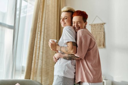 Téléchargez les photos : Un couple lesbien aux cheveux courts serrant tendrement devant une fenêtre, mettant en valeur leur amour et leur proximité. - en image libre de droit