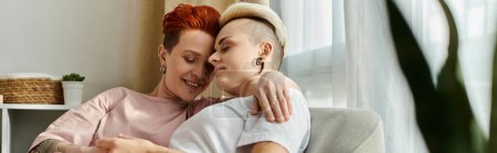 Foto de Dos personas, una pareja lesbiana de pelo corto, se abrazan amorosamente en un acogedor sofá en una cálida sala de estar. - Imagen libre de derechos