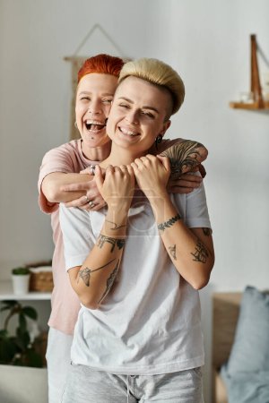 Foto de Dos mujeres con el pelo corto compartiendo un abrazo sincero en una acogedora sala de estar, expresando amor y conexión. - Imagen libre de derechos