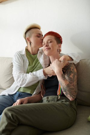 A touching scene of two women with short hair embracing each other warmly on a comfy couch at home.