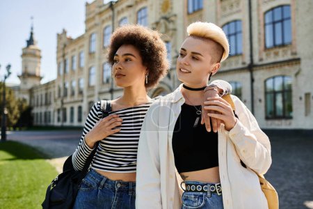 Foto de Dos mujeres jóvenes están de pie con confianza frente a un edificio moderno en un campus universitario. - Imagen libre de derechos