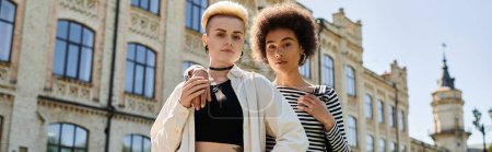 Téléchargez les photos : Un jeune couple lesbien multiculturel portant des vêtements élégants et décontractés pose élégamment devant un bâtiment. - en image libre de droit