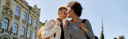 Téléchargez les photos : Deux jeunes femmes, un couple lesbienne multiculturel, expriment leur amour avec un baiser dans la rue près d'un campus universitaire. - en image libre de droit
