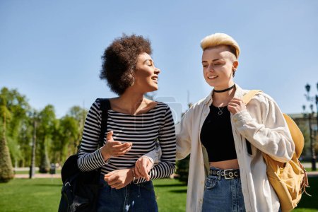 Two young women, a multicultural lesbian couple, in stylish attire chatting in a park near a university campus.