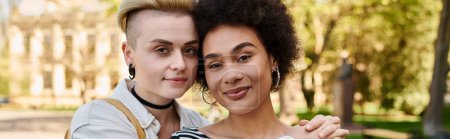 Téléchargez les photos : Deux jeunes femmes s'embrassent chaleureusement devant un parc verdoyant par une journée ensoleillée, montrant leur lien et leur amitié. - en image libre de droit