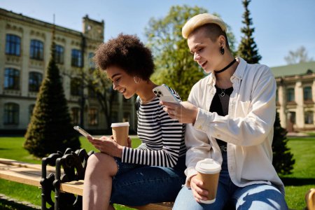 Dos mujeres jóvenes con atuendo casual sentadas en un banco, absortas en sus teléfonos celulares.