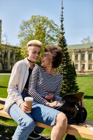 Zwei junge Leute, ein multikulturelles lesbisches Paar, sitzen auf einer Bank in einem Park und genießen an einem sonnigen Tag Gesellschaft.