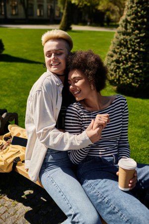 Foto de A young multicultural lesbian couple relaxes on a park bench, enjoying a moment of peace together. - Imagen libre de derechos