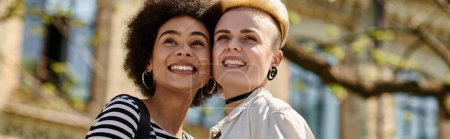 Deux jeunes femmes, un couple lesbienne multiculturel, partagent des sourires joyeux devant un bâtiment universitaire.