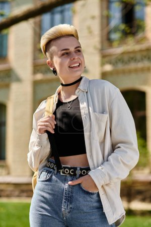 Young woman confidently struts in jeans and a t-shirt, showcasing her shaved head outdoors on a university campus.