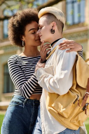 una pareja lésbica multicultural, abrazándose frente a un edificio universitario.