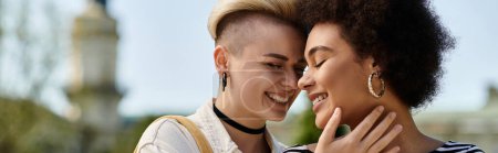 Foto de Dos mujeres, una joven pareja lesbiana multicultural, se abrazan frente a un edificio vibrante en un campus universitario. - Imagen libre de derechos