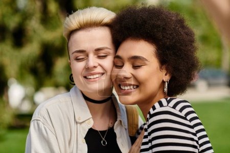 Two young women in stylish attire sharing a heartfelt hug in a vibrant park setting.
