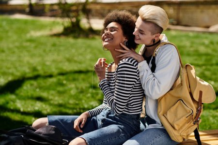 Ein multikulturelles lesbisches Paar in stylischer Kleidung sitzt auf einer Bank in einem Park und ist an einem sonnigen Tag in Gespräche vertieft.