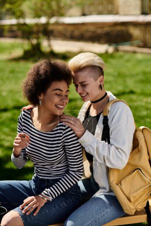 Foto de Two young women, lesbian couple, sit peacefully on a bench in a park, surrounded by lush greenery and the sounds of nature. - Imagen libre de derechos