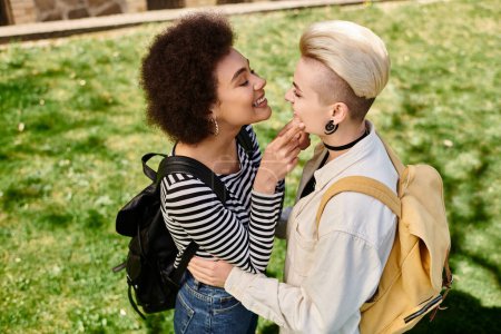 Foto de Dos mujeres jóvenes, vestidas con estilo, comparten un abrazo sincero y se besan en un campo de hierba. - Imagen libre de derechos