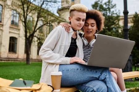 Foto de Two young women in casual clothing sitting on a bench, engrossed in their laptop screen. - Imagen libre de derechos