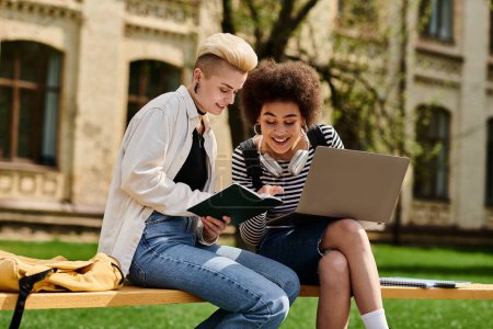Foto de Two young women, stylishly dressed, working together on a laptop while sitting on a bench outdoors. - Imagen libre de derechos