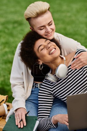 Deux jeunes femmes assises sur l'herbe avec un ordinateur portable, profitant du plein air tout en travaillant ou en étudiant ensemble.