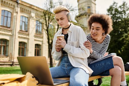 Zwei Frauen in Freizeitkleidung sitzen auf einer Bank, konzentrieren sich auf den Laptop-Bildschirm und arbeiten gemeinsam im Freien.