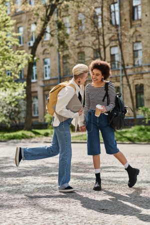 Photo for Stylish, casual, multicultural lesbian couple stroll on city street near university campus. - Royalty Free Image