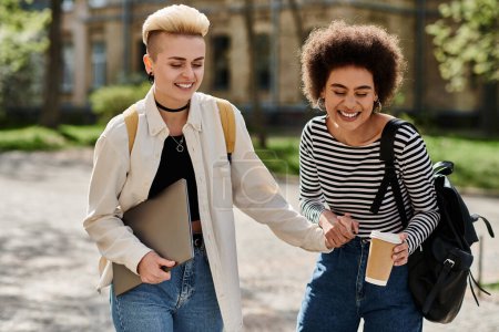 Jeune couple lesbienne multiculturel, élégant et décontracté, se tenant la main tout en marchant dans une rue du campus universitaire.