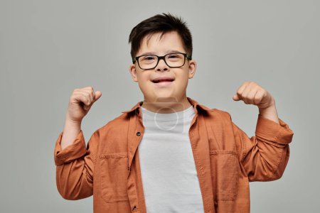 little boy with Down syndrome flexing his arms proudly against a gray background.