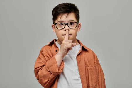 little boy with Down syndrome with glasses making a hush sign.