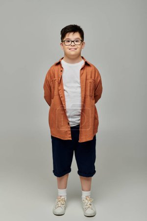 little boy with Down syndrome in glasses and shorts, standing confidently against gray background.