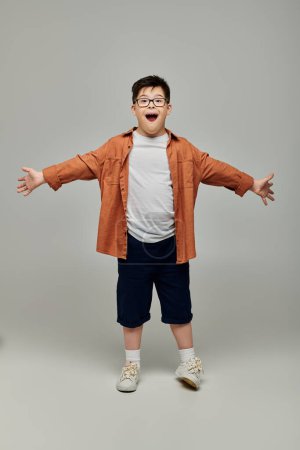 little boy with Down syndrome, arms outstretched, against gray background.