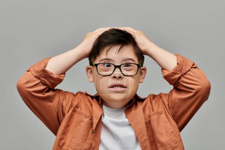 A little boy with Down syndrome with glasses is holding his head up in contemplation.