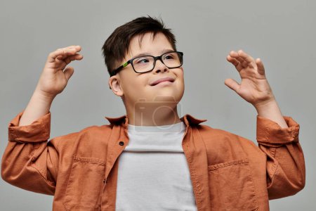 little boy with Down syndrome with glasses joyfully raises his hands in the air.