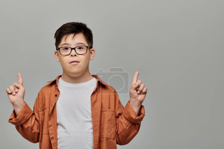 Un niño pequeño con síndrome de Down con gafas gestos juguetones con el dedo.