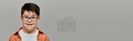 Photo for Cheerful boy with Down syndrome smiling in front of gray backdrop. - Royalty Free Image