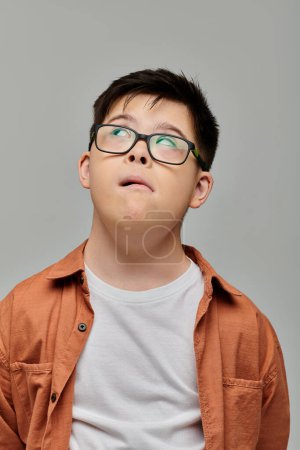Un niño pequeño con síndrome de Down con gafas mira hacia arriba, su expresión curiosa y atractiva.
