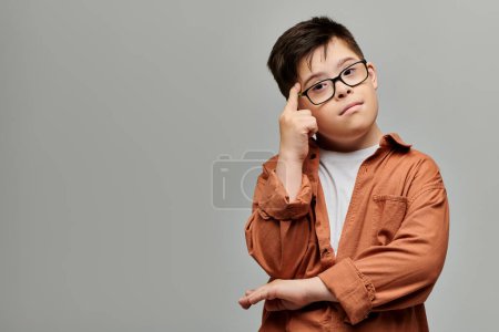 Adorable boy with Down syndrome posing thoughtfully with hand on head.