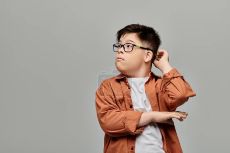 A lively little boy with Down syndrome wearing glasses poses on a gray background.