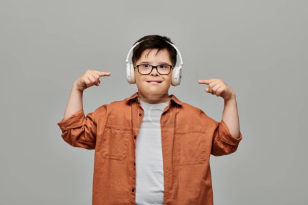 Kleiner Junge mit Down-Syndrom trägt Kopfhörer und zeigt auf seine Ohren.