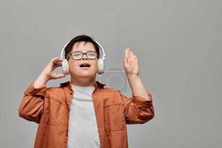 Téléchargez les photos : Un petit garçon trisomique écoute joyeusement de la musique à travers des écouteurs. - en image libre de droit
