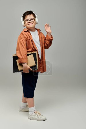 Foto de Niño pequeño con síndrome de Down usando auriculares, sosteniendo libros. - Imagen libre de derechos