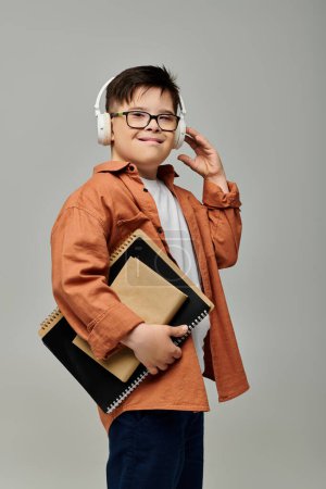Téléchargez les photos : Petit garçon avec le syndrome de Down portant des écouteurs, tenant des carnets. - en image libre de droit