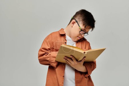A little boy with Down syndrome with glasses reads a book intently.