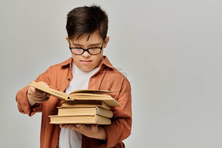 A boy with Down syndrome with glasses holds a stack of books.