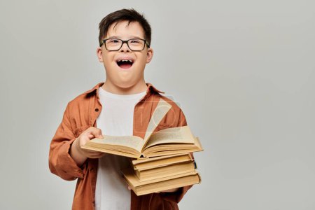 little boy with Down syndrome with glasses cheerfully holds a tall stack of books.