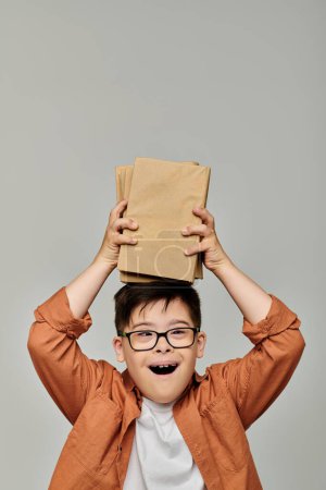 Foto de Lindo chico con síndrome de Down juguetonamente sosteniendo pila de libros. - Imagen libre de derechos