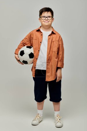 Kleiner Junge mit Down-Syndrom hält mit Brille einen Fußball.