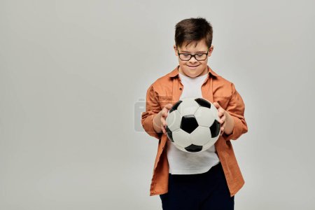 A boy with Down syndrome with glasses holds a soccer ball